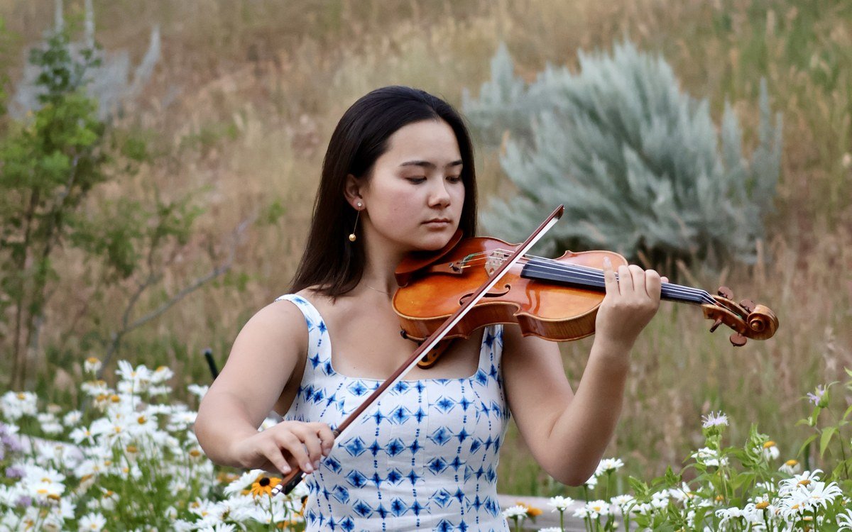 Mari Roes performing violin outdoors among wildflowers